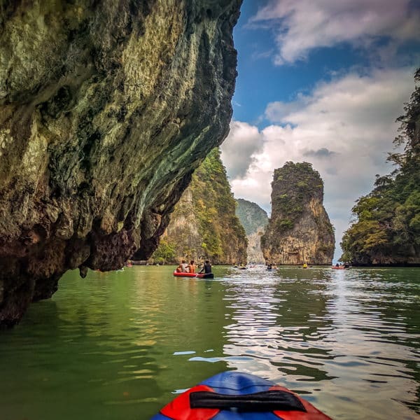 a red kayak navigates closely past a limestone cliff at james bond island